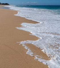 Exhausted waves climbing up the sandy slope and separating into interesting shapes of white foam against the yellow sand, Polihale Beach State Park, Kauai, Hawaii
