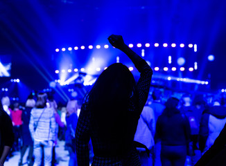 Silhouette of a dancing girl at a concert among a crowd of spectators.