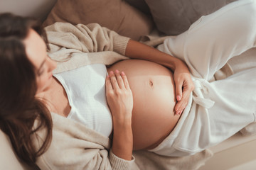 Careless lady lying and holding her hands on pregnant belly - obrazy, fototapety, plakaty