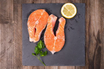 Two fresh raw salmon steaks with lemon and parsley on rustic table