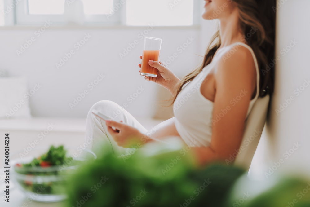 Wall mural calm expectant mother sitting with juice and cellular on kitchen