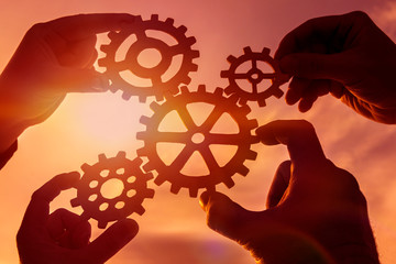 gears in the hands of people on the background of the evening sky. mechanism, interaction, teamwork.