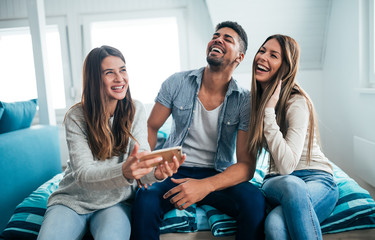 Friends at home having a blast. Three friends laughing while sitting on sofa.