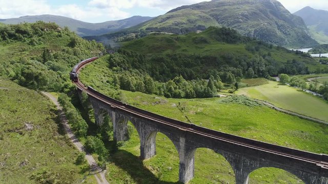 Drone shot of classic steam train crossing the famous historic Glenfinnan viaduct, travel and tourism Scotland