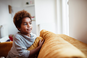 Beautiful little african american girl on sofa, looking away.