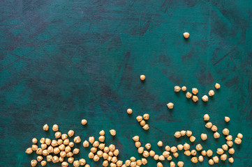 Dry chickpea beans are freely scattered on an emerald green background.