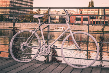 Fototapeta na wymiar Old abandoned bicycle covered with white paint. European city view with bicycle on a bridge and river.