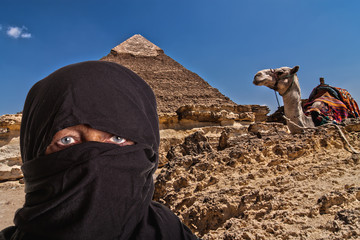 portrait of a black veiled woman with camel and pyramid in Egypt