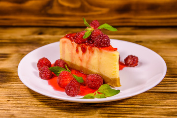 White plate with cheesecake New York, leaves of mint and raspberries on wooden table