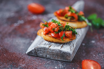 Italian bruschetta with tomatoes and herbs on a wooden board on a dark background