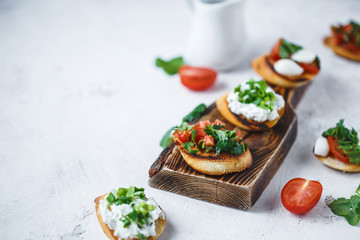 several types of italian bruschetta with tomatoes, mozzarella and herbs on a wooden board on a light background