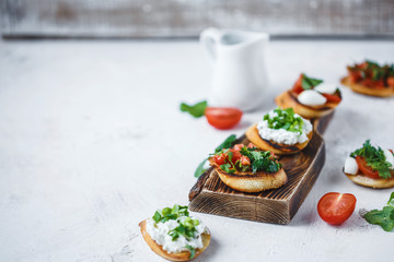 several types of italian bruschetta with tomatoes, mozzarella and herbs on a wooden board on a light background