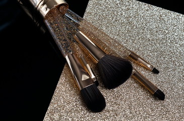 Makeup brushes set in gold color on gold black background. Professional makeup tools . Women accessories.  Copy space
