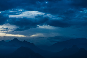 Amazing night landscape of calm clouds, blue sky and silhouettes of high mountains. Horizontal color photography.