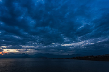 Beautiful sunset cloudy sky and dark sea water with silhouettes of mountains in background. Night is coming. Horizontal color photography. - Powered by Adobe
