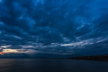 Fotobehang Nacht Mooie zonsondergang bewolkte hemel en donker zeewater met silhouetten van bergen op de achtergrond. De nacht komt eraan. Horizontale kleurenfotografie.