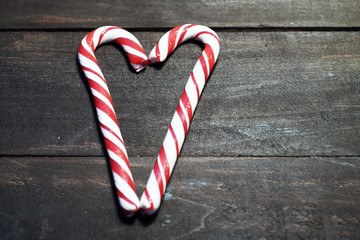 Red and white candy canes forming a heart on a background of dark wooden planks. Close up. Christmas photo 