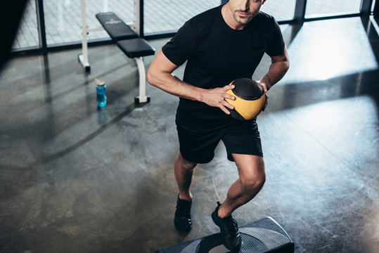 cropped image of sportsman training on step platform with medicine ball in gym