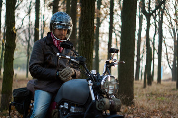 Man and old custom cafe-racer Motorcycle on forest  at sunset