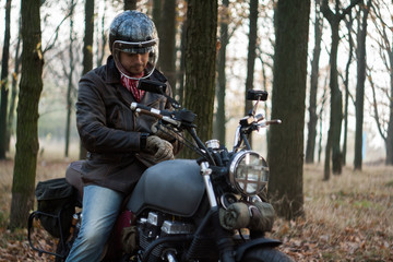 Fototapeta premium Man and old custom cafe-racer Motorcycle on forest at sunset