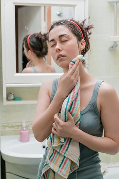 cute girl wipes her face with a towel after water treatments standing in front of a mirror