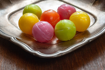 Candy balls. Colored dragee hard fruit candies stacked on a silver saucer, wooden background.