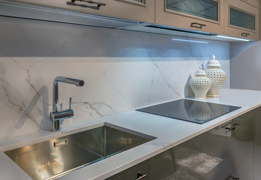Fragment of the interior of modern cuisine. Marble table top with tap, metal sink and induction hob