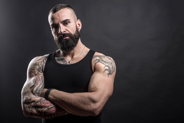 Uomo muscoloso e tatuato con braccia conserte guarda deciso in macchina - sfondo nero