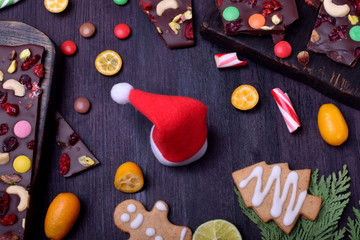 Santa Claus hat surrounded by chocolate, gingerbread cookies, citrus fruits and candy canes. Christmas composition