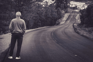 Active senior man standing on lonely road between mountains