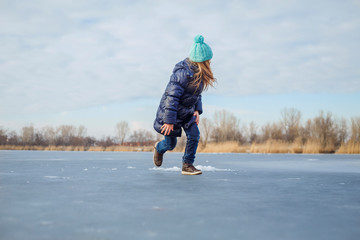 Cute little girl wearing navy jacket and knitted hat walking in winter park. Pretty child playing and jumping on frozen lake. Family vacation with kid on christmas holidays	