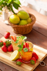 Refreshing summer drink with lemon, strawberry and mint on wooden table