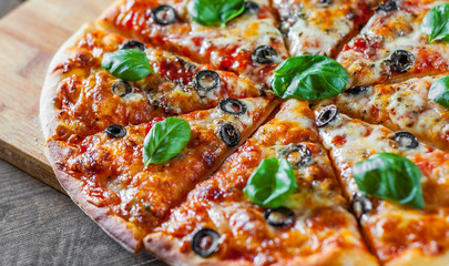 sliced Pizza with Mozzarella cheese, Tomatoes, pepper, olive, Spices and Fresh Basil. Italian pizza. Pizza Margherita or Margarita on wooden table background