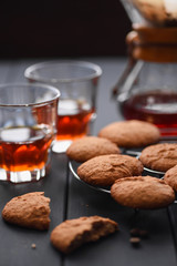 Healthy oatmeal cookies with filtered drip coffee made in pour-over gadget served in glasses on dark background
