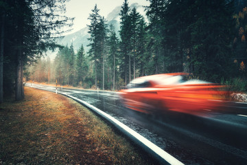 Blurred red car in motion on the road in autumn forest in rain. Perfect asphalt mountain road in...