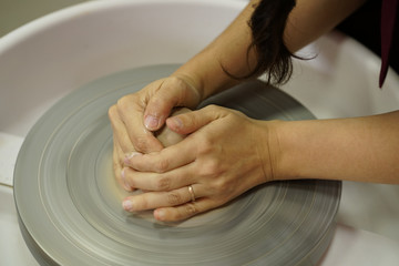 woman makes a jug with dirty arms on a Potter's wheel from raw wet clay