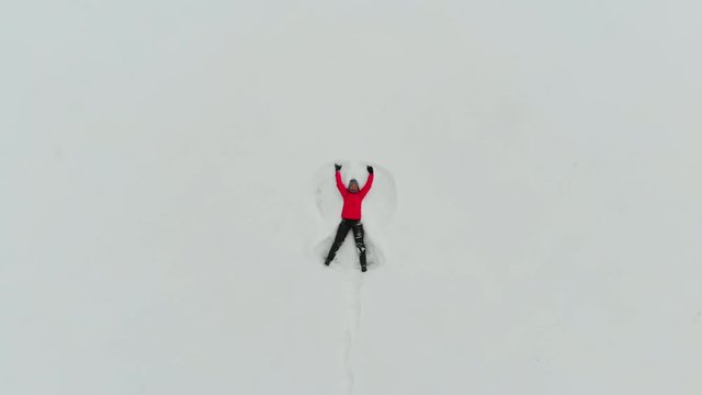 Woman making snow angel. Aeriel view from the drone. Flying over young cheerful girl making snow angels in winter.