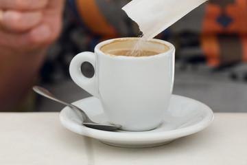 sugar is poured into a cup of coffee