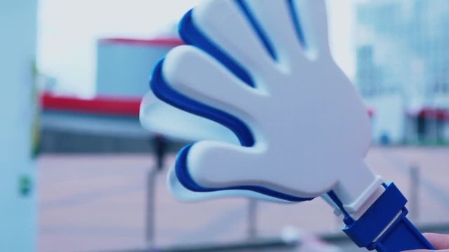 Children's hand holding a fan rattle. Football attributes. White-blue palm-rattle. The child supports his team.
