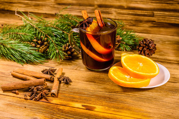 Cup of mulled wine with cinnamon, sliced orange and fir tree branches on wooden table