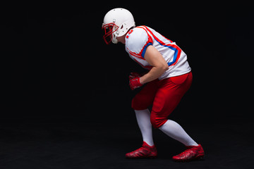 Side view of American football player wearing helmet taking position while playing against black...