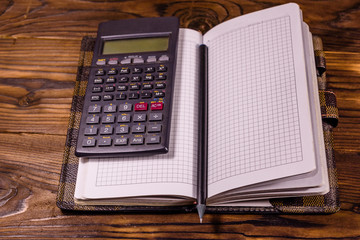 Opened notepad, scientific calculator and pencil on wooden table