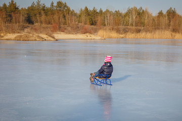 Fototapeta na wymiar Pretty little girl wearing navy jacket and knitted hat playing in a snowy winter park. Child sledding on ice on a frozen lake. Family vacation with kid in snowy season