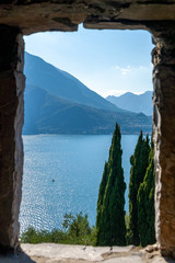 View on a blue mountain lake with green cypresses through the stone window in the early sunny evening - 240042488