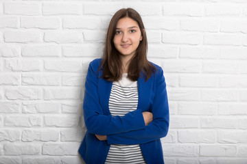 A young pretty smiling girl against a white loft-style brick wall. She looks at the viewer. Copy space.