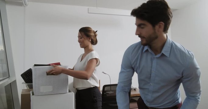 Young latin business woman holding boxes and moving in new office with man. White businesswoman preparing working room to start new job, colleague helping her. Female manager at work with coworker