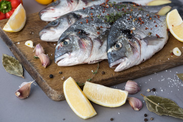 Four sea dorado fish with fragrant spices lie on a wooden board with a large wooden spoon of salt. Cooking process