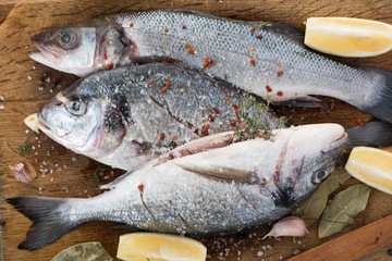 Sea dorado fish with fragrant spices lie on a wooden board with a large wooden spoon of salt. Cooking process
