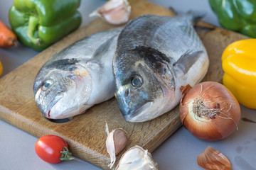 Two large fish dishes of Mediterranean cuisine on a wooden board on the background of onion, tomato, sweet pepper. Cooking process.