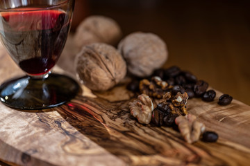 Red wine glass with nuts and coffee beans on the desk made from olive tree with contrast picture on the surface in morning sun rays